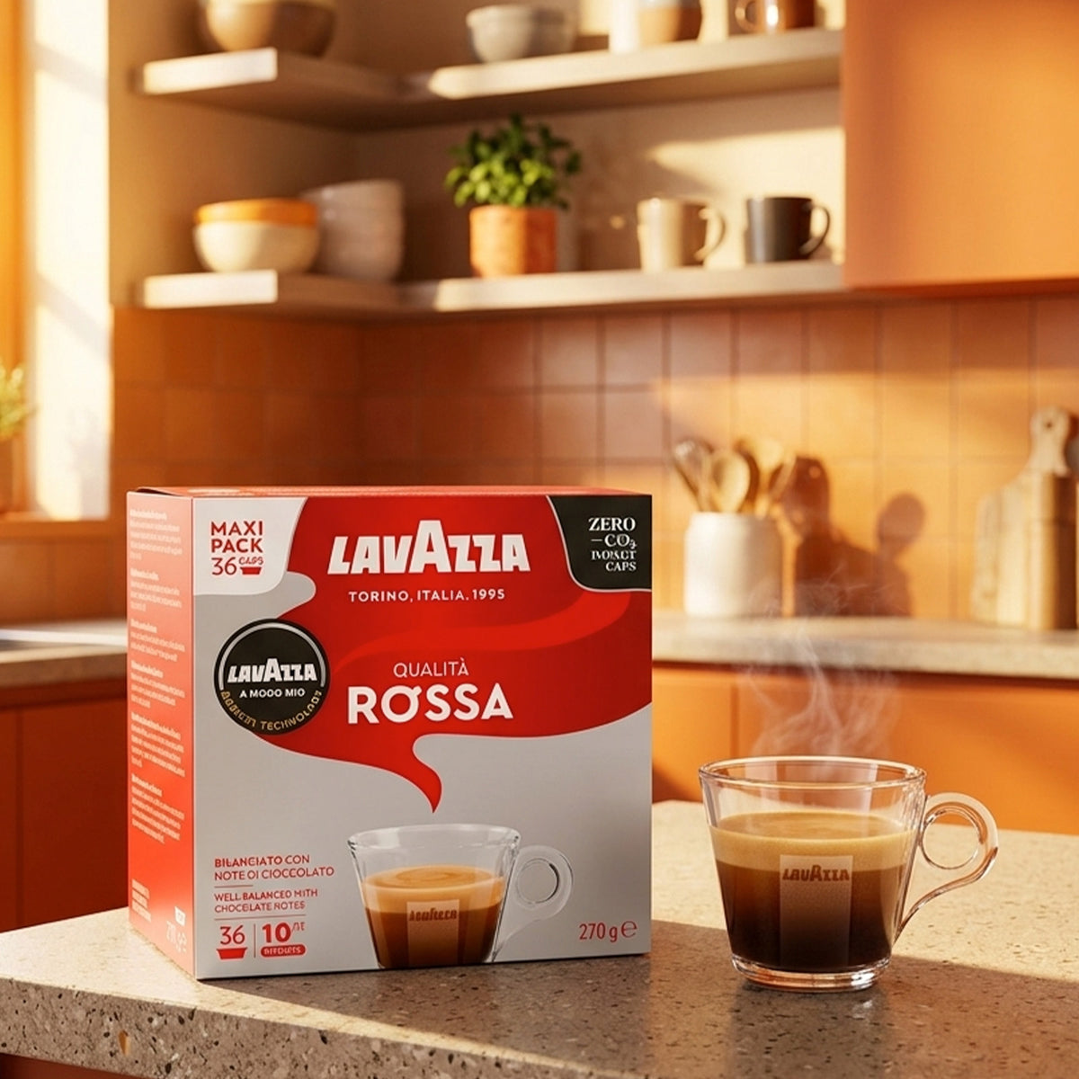 A box of Lavazza Qualità Rossa coffee capsules sits on a kitchen counter next to a steaming glass cup of espresso, with a warm kitchen interior in the background.