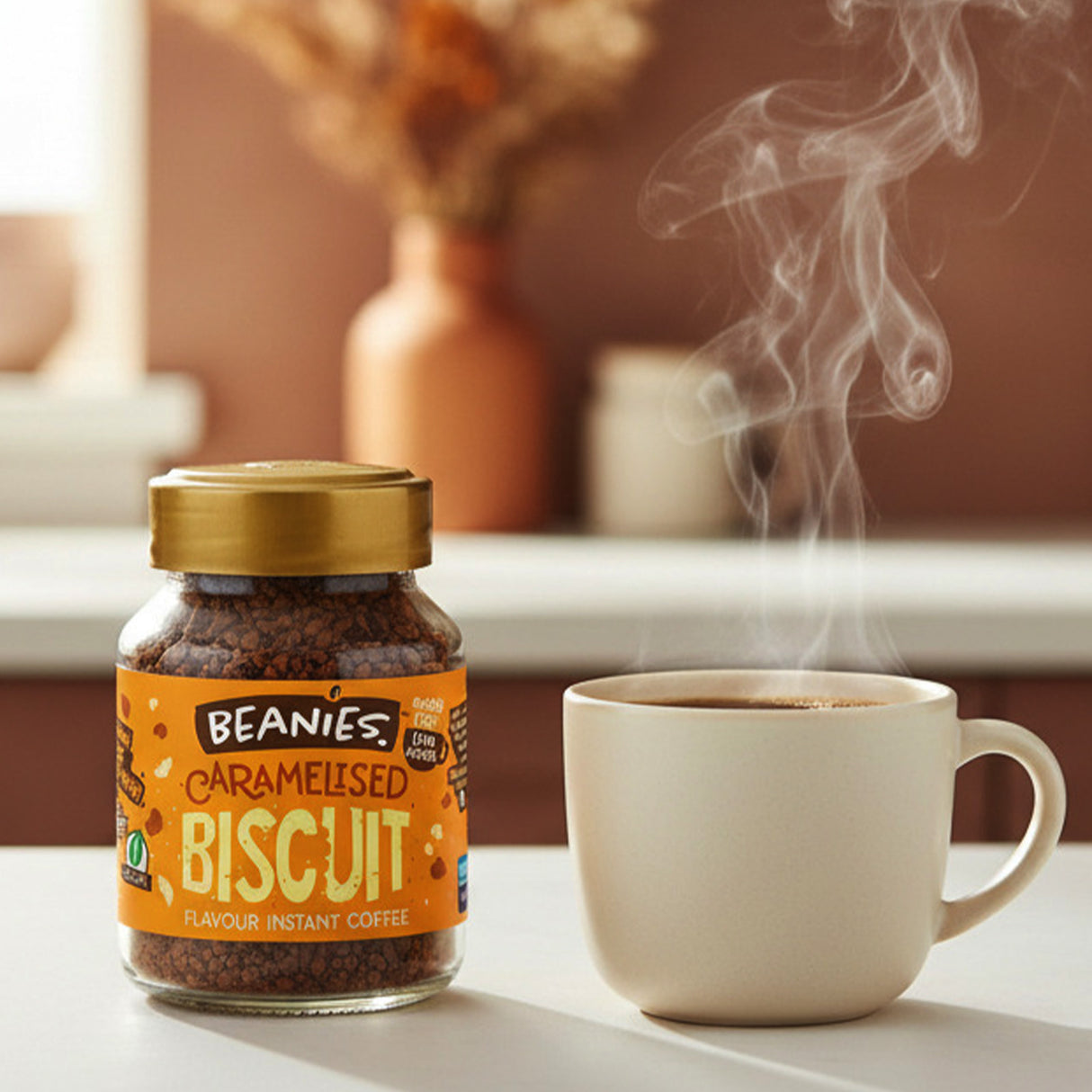 Jar of Beanies Caramelised Biscuit instant coffee with a steaming cup on a table.