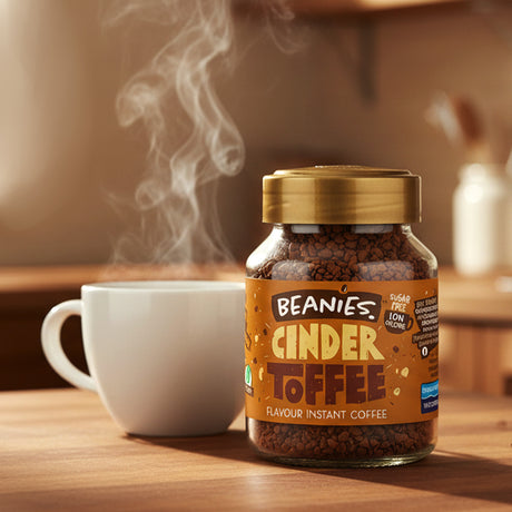Jar of Beanies Cinder Toffee instant coffee with a steaming cup on a wooden surface