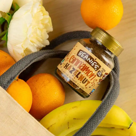 Jar of 'Beanie's Cinnamon Hazelnut' coffee in a bag with fruits on a wooden surface