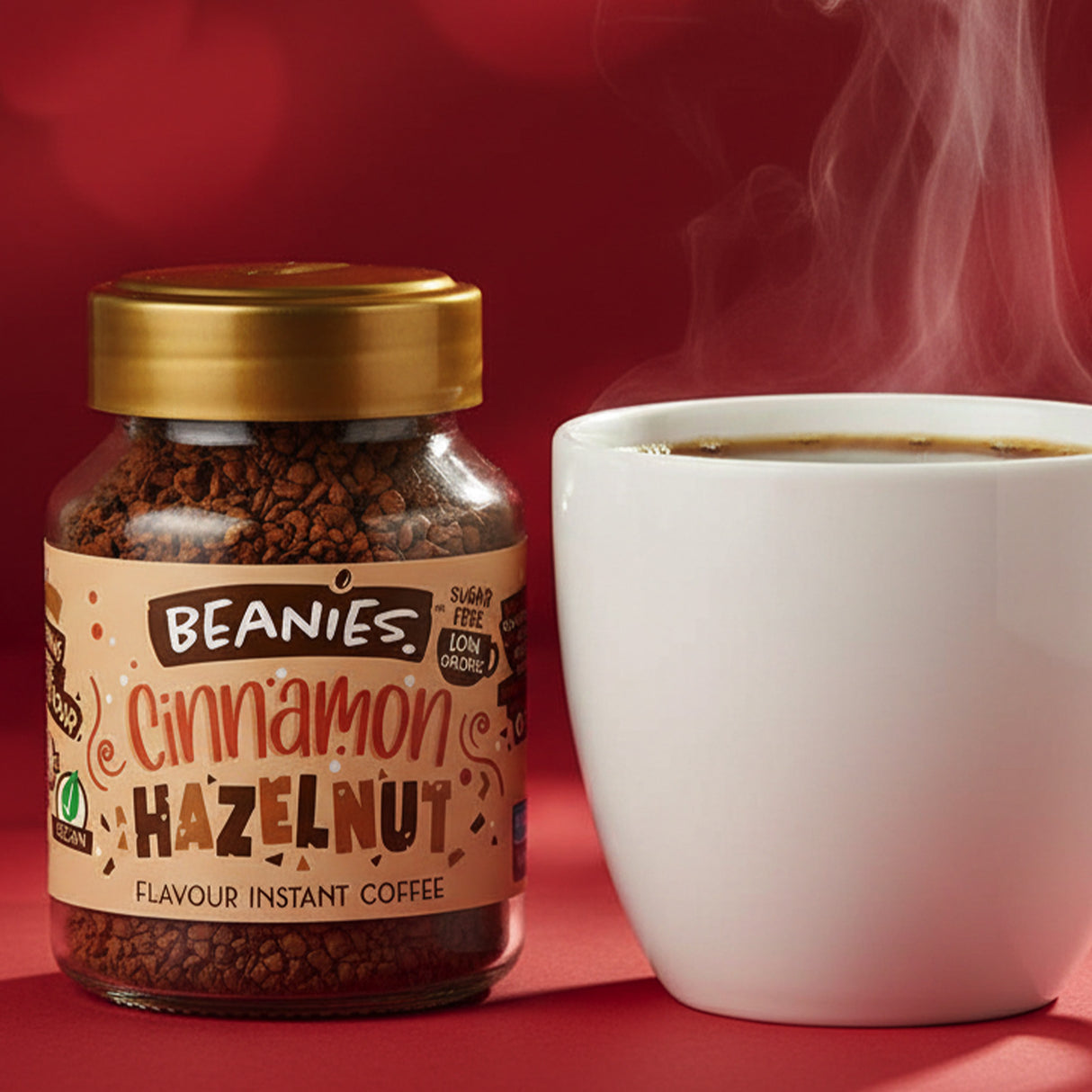 Jar of Beanies Cinnamon Hazelnut instant coffee with a steaming white cup on a red background