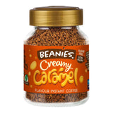 Jar of Beanies Creamy Caramel instant coffee on a wooden table with a steaming cup of coffee.