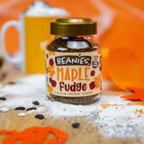 Jar of Beanies Maple Fudge instant coffee on a wooden surface with an orange background
