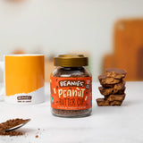 Jar of Beanies Peanut Butter Cup instant coffee with a spoonful of coffee grounds and a stack of cookies on a white surface.