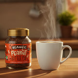 Jar of Beanies Peanut Butter Cup instant coffee next to a steaming white mug on a wooden surface.