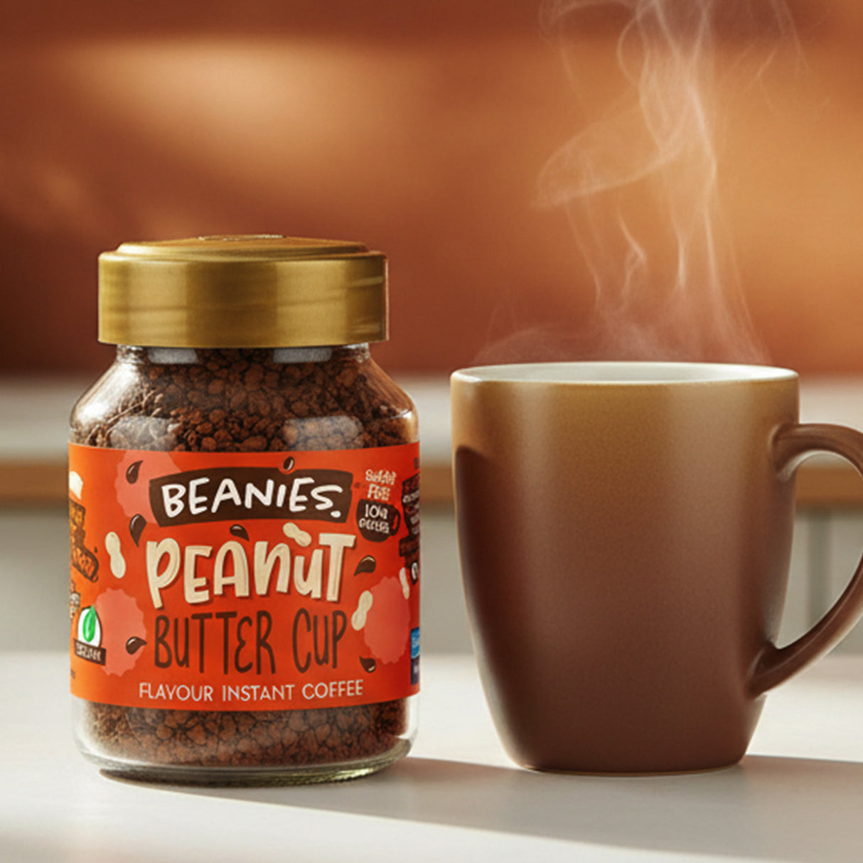 Jar of Beanies Peanut Butter Cup instant coffee next to a steaming cup on a wooden surface.