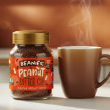 Jar of Beanies Peanut Butter Cup instant coffee next to a steaming cup on a wooden surface.