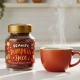 Jar of Beanies Pumpkin Spice instant coffee with a steaming cup on a light surface.