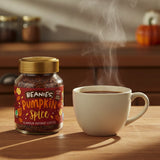 Jar of Beanies Pumpkin Spice instant coffee next to a steaming cup on a wooden table.
