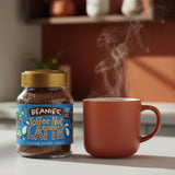 Jar of Beanies Toffee Nut Latte instant coffee next to a steaming red mug on a blurred kitchen background.