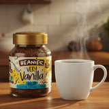 Jar of Beanies Very Vanilla Decaf instant coffee with a steaming white mug on a wooden surface.