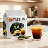 Tassimo coffee pod packaging with a glass of coffee on a kitchen counter.
