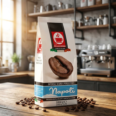 A bag of Napoli espresso coffee beans stands on a wooden table in a kitchen setting, with scattered coffee beans around the base and a blurred espresso machine and shelves in the background.